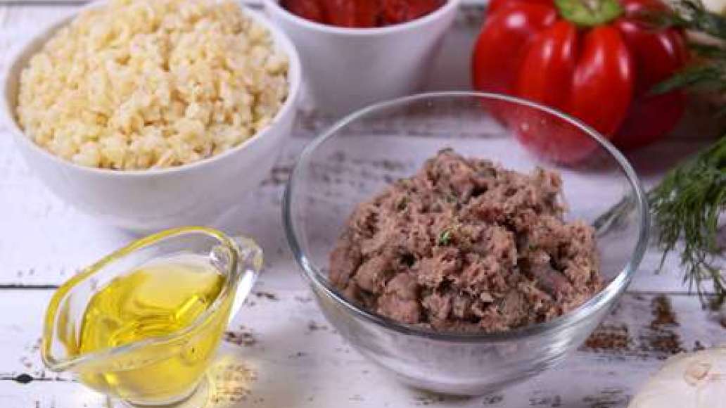 Пропустите лук через мясорубку, измельчите зелень и смешайте с фаршем. Добавьте соль и перец. Отварите булгур до полуготовности согласно инструкции. Разделите капусту на листья. Вскипятите в кастрюле воду, добавьте соль и опустите в неё капустные листья, 
