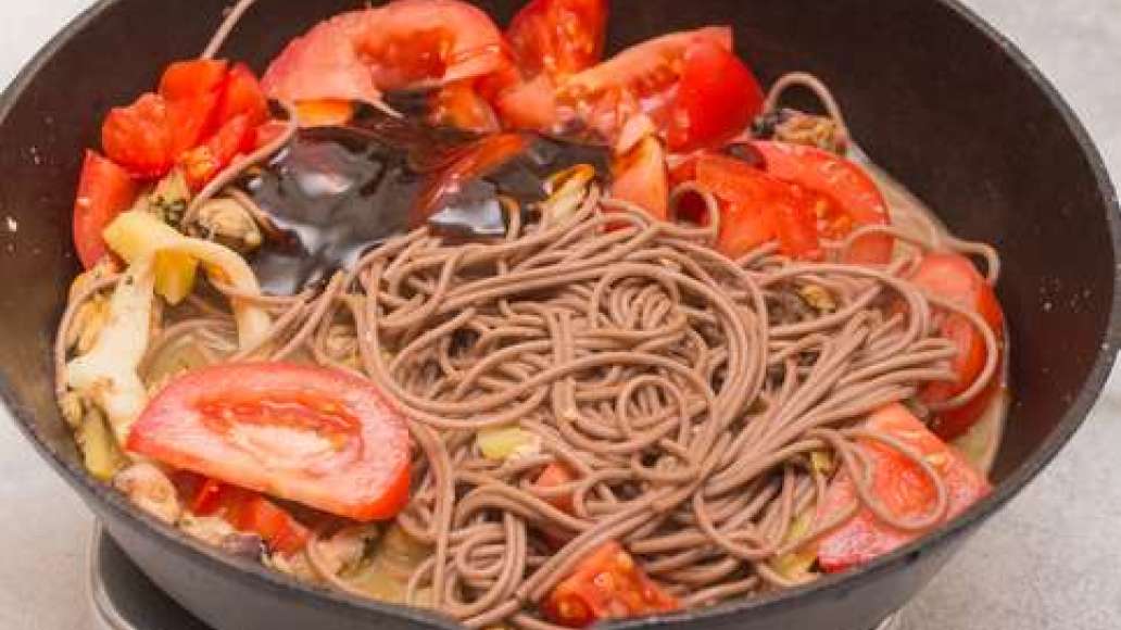Добавить в сковородку к морепродуктам гречневую лапшу, нарезанные помидоры, соус терияки, энергично перемешивая, довести до готовности.