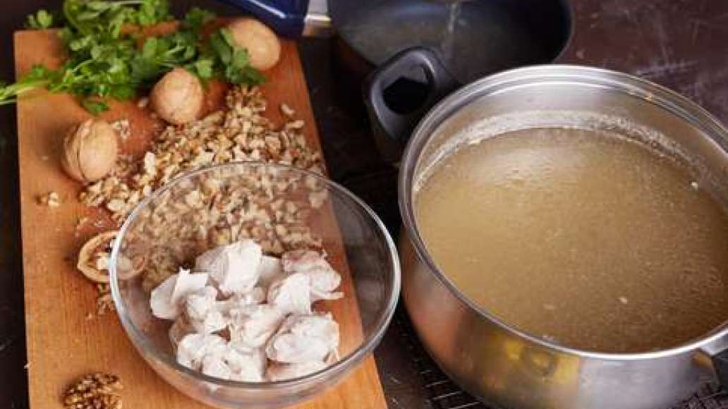 Залить индейку водой и сварить бульон. Вынуть мясо, бульон процедить через частое сито.  Измельчить орехи.
