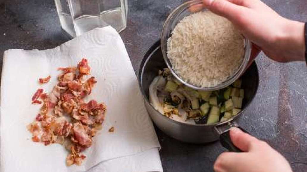 Собрать в кастрюле ингредиенты: цукини, морепродукты и рис. Залить водой и довести до кипения. Бекон обжарить и выложить на салфетку. 