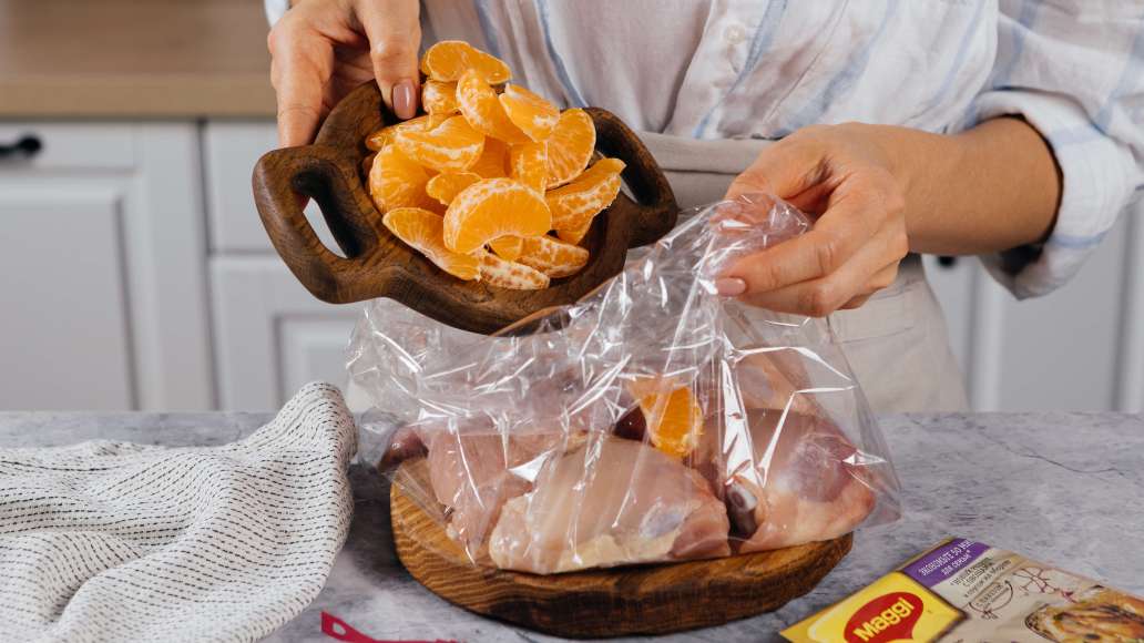 Достать из пачки MAGGI® НА ВТОРОЕ для сочной курицы с чесноком пакет и развернуть. Поместить в пакет бедра и дольки мандаринов.