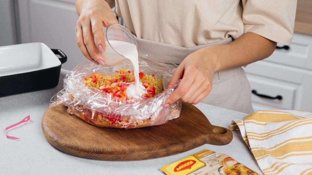 Достать из пачки MAGGI® НА ВТОРОЕ для сочной курицы карри пакет и развернуть. Положить в пакет ножки, помидоры, булгур. Добавить воду и сливки.