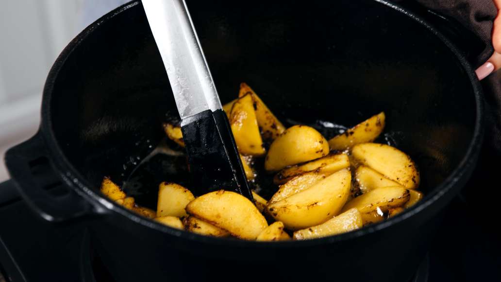 Картофель очистить и нарезать средними дольками. Готовое мясо переложить на бумажные полотенца. В том же жиру обжарить картофель до румяной корочки и мягкости, периодически помешивая.