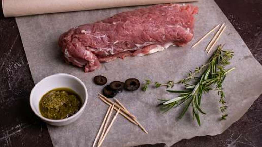На мясо выложить маслины и пряные травы, посыпать сушёными помидорами. Свернуть рулетом, обвязать нитью или сколоть деревянными шпажками. Обмазать рулет соусом песто и плотно завернуть в пергамент. Поместить в духовку и запекать 30–35 минут.
