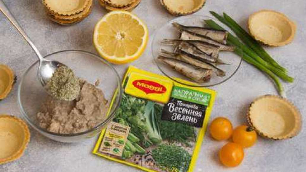 Шпроты соединить с MAGGI® Приправа Весенняя зелень, лимонным соком  и помидорами черри и наполнить тарталетки. Зеленый лук мелко нарезать. 