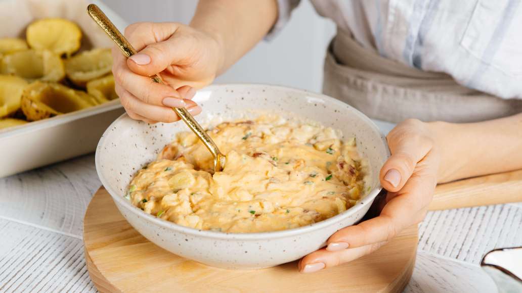 Добавить к мякоти картофеля сыр, лук, бекон, сметану, масло и молоко (немного сыра и бекона отложить для украшения). Тщательно перемешать до образования кремообразной массы. 

