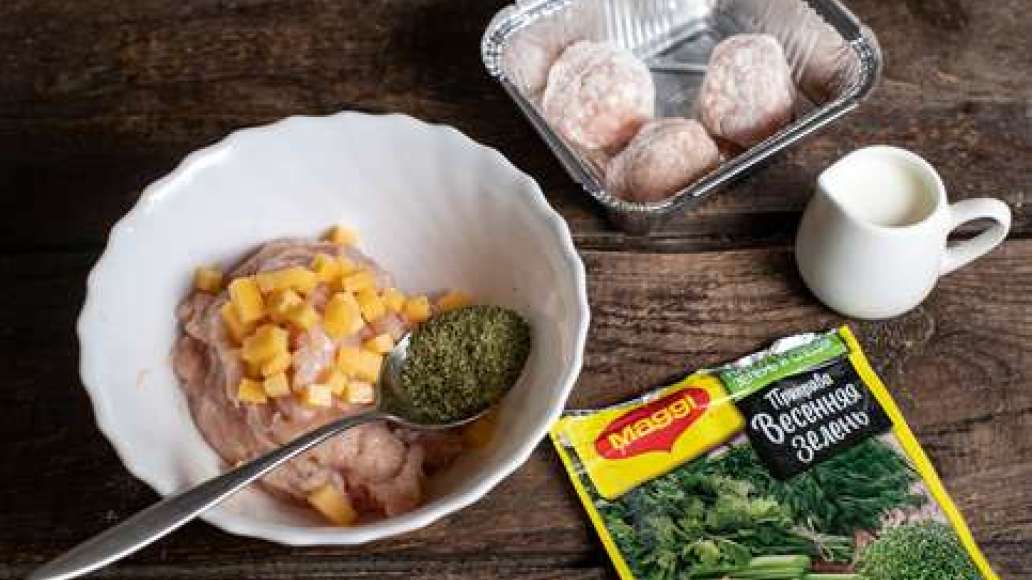 Соединить  фарш с MAGGI® Приправа Весенняя зелень, добавить кубики сыра и чеснок и тщательно перемешать.  Сформировать небольшие круглые фрикадельки. Обвалять в муке, стряхнуть излишки.  Смазать растительным маслом жаропрочную форму и выложить фрикадельки