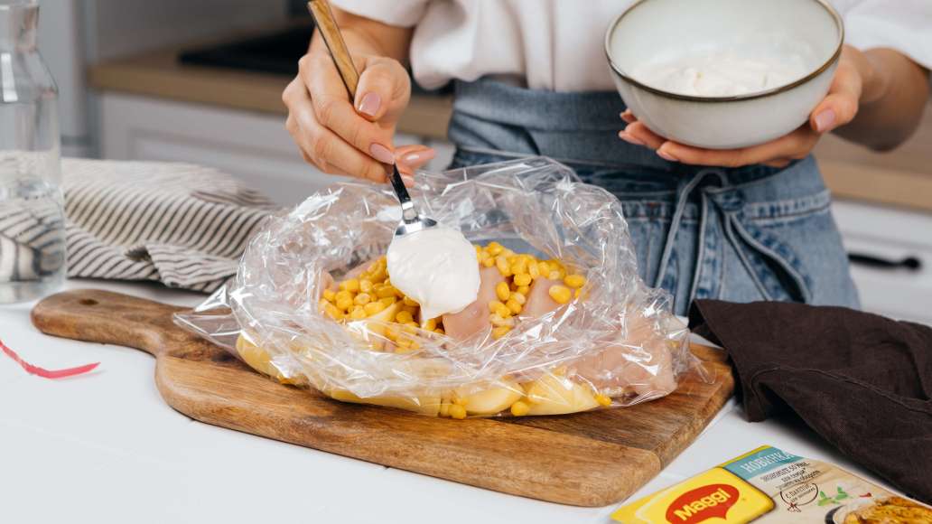 Достать пакет из пачки MAGGI® На Второе для сочных куриных грудок в соусе три сыра и развернуть. Положить в него картофель, курицу, кукурузу, затем добавить сметану и воду.