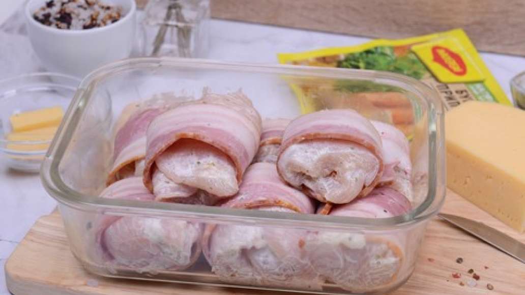 Приготовьте рулетики: положите сыр на середину куриной пластины и сверните её так, чтобы сыр не торчал. Оберните рулет ломтиком бекона и положите в форму для запекания.