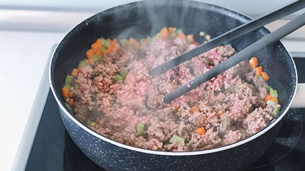 Добавить в овощную смесь мясной фарш, распределяя его деревянной лопаткой или кулинарными щипцами по всей сковороде.