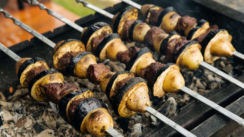 Насадить на шампуры мясо, перемежая куски клубнями картофеля и кружками баклажана. Жарить над прогоревшими углями до появления на мясе насыщенной румяной корочки и мягкости овощей, часто переворачивая.