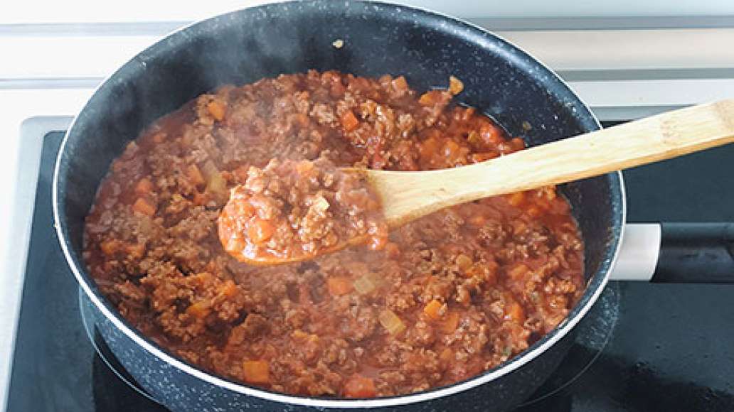 Когда фарш полность поменяет цвет и обжарится, добавить к мясному рагу готовый томатный соус для болоньезе и все перемешать. Убавить огонь до среднего и тушить под крышкой 15 минут.