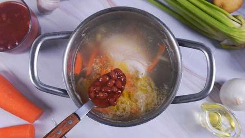 Добавьте зажарку и фасоль в кастрюлю с курицей. Разрежьте стебли сельдерея на крупные кусочки, помидор и очищенный картофель нарежьте  кубиками, измельчите чеснок.