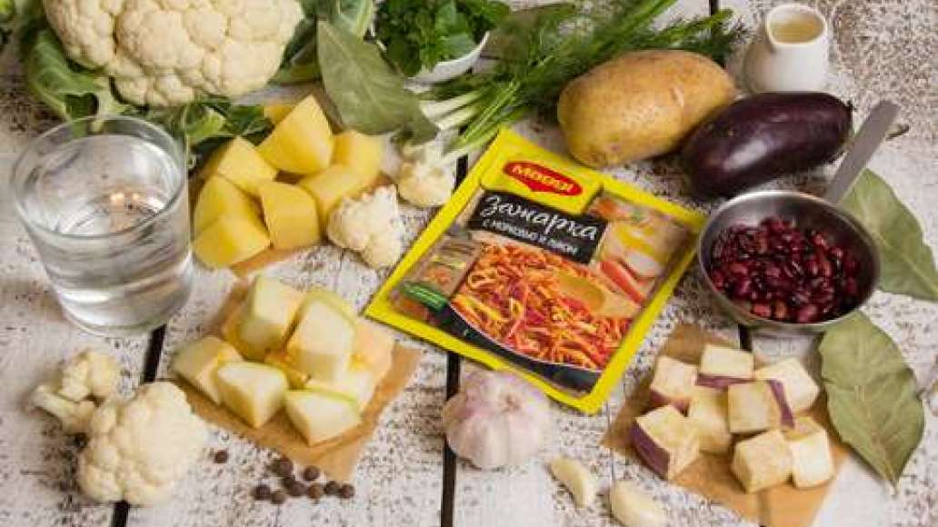 Картофель, кабачок и баклажан очистить и нарезать крупными кубиками. Цветную капусту разобрать на соцветия. Фасоль сварить и слить отвар. Чеснок пропустить через пресс. Укроп, зеленый лук и базилик мелко нарезать. 