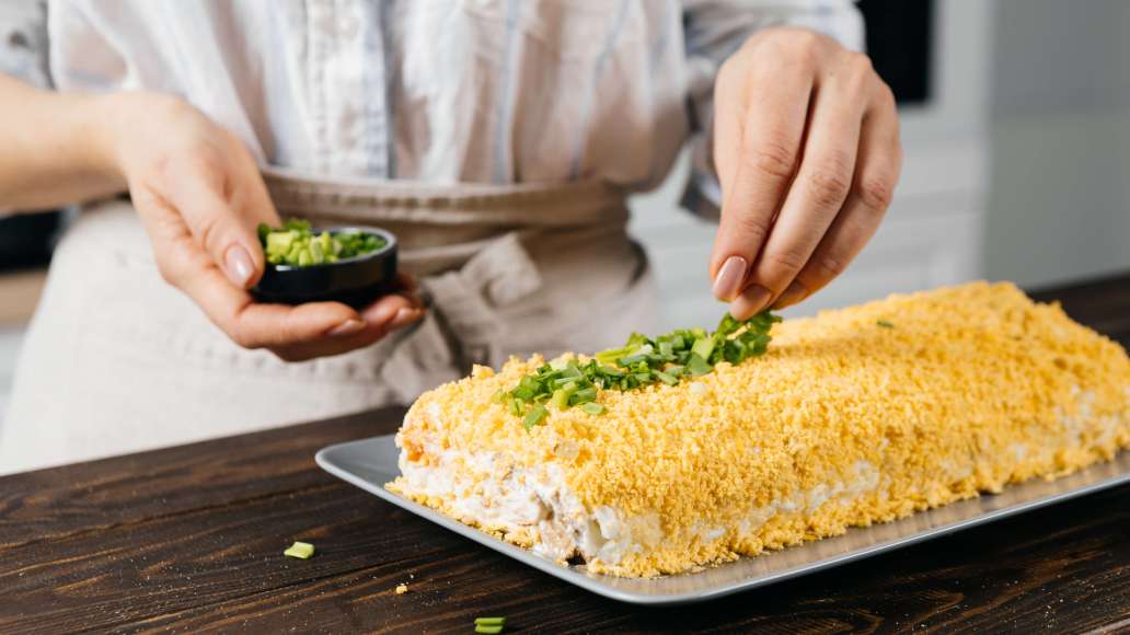 Аккуратно удалить пищевую плёнку. Украсить салат тёртыми желтками, зелёным луком и подавать.