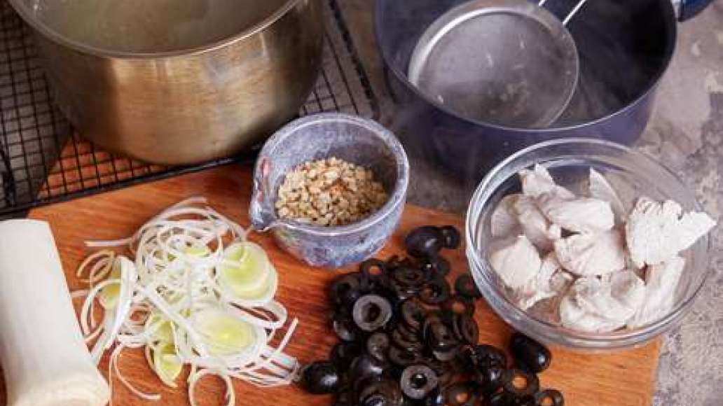 Залить индейку водой и сварить бульон. Вынуть и остудить мясо, бульон процедить. Измельчить орехи. Лук-порей нарезать тонкими кольцами. Маслины нарезать колечками.