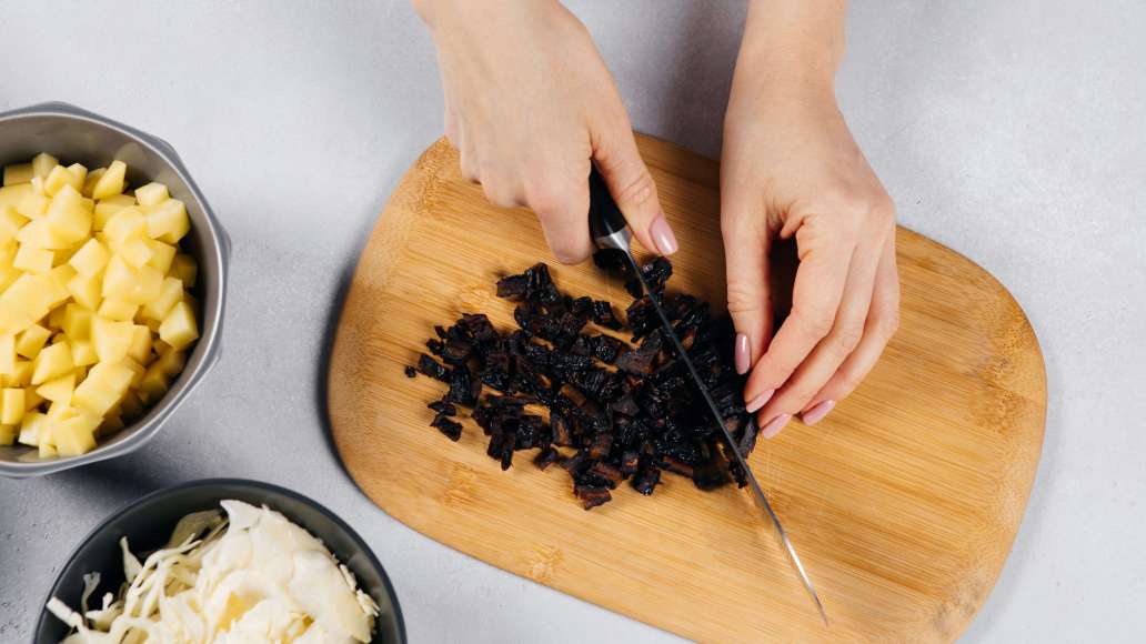 Готовое мясо вынуть из бульона. Очищенный картофель нарезать кубиками среднего размера. Капусту тонко нашинковать, чернослив мелко нарезать. Добавить в бульон и варить 10-15 минут.