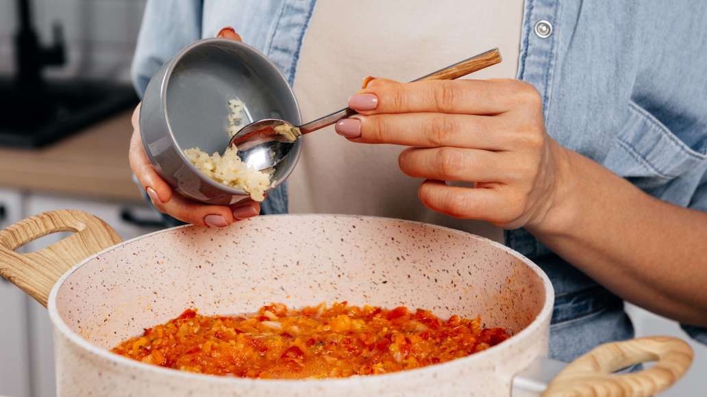 Попробовать аджику на вкус и при необходимости добавить соли и сахара. Добавить чеснок, уксус, перемешать и варить еще 5 минут.