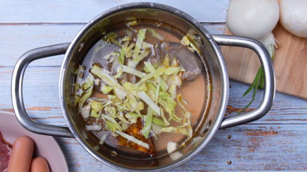 В это время поставьте мясной бульон на огонь, доведите до кипения. Нашинкуйте капусту и добавьте в кипящий бульон, варите 10 минут. 