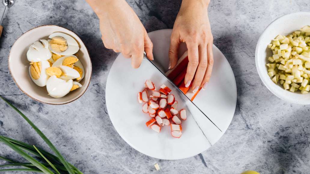 Нарезать кусочками крабовые палочки, шампиньоны — пластинками, мелко нарезать зелёный лук.
