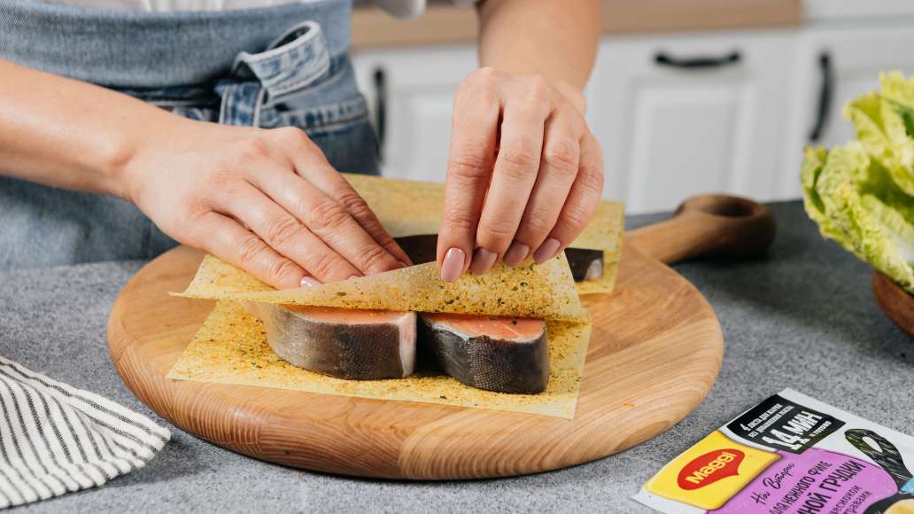 Уложить рыбу на раскрытые листы MAGGI® НА ВТОРОЕ для нежного филе куриной грудки с чесноком и травами. Накрыть сверху свободными половинками листов.