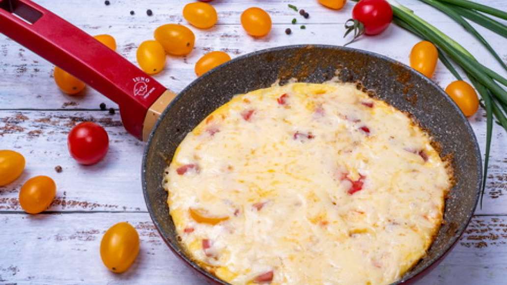 Смешайте яйца с колбасой, сосиской, помидором и луком. В разогретую сковороду положите масло. Вылейте омлетную смесь и накройте крышкой. Натрите сыр и посыпьте им омлет. Сверху добавьте зелень.